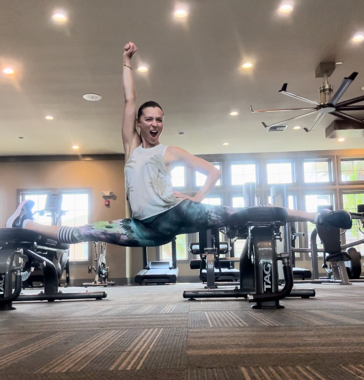 Nadya performing a full split across two gym benches, arm raised in celebration